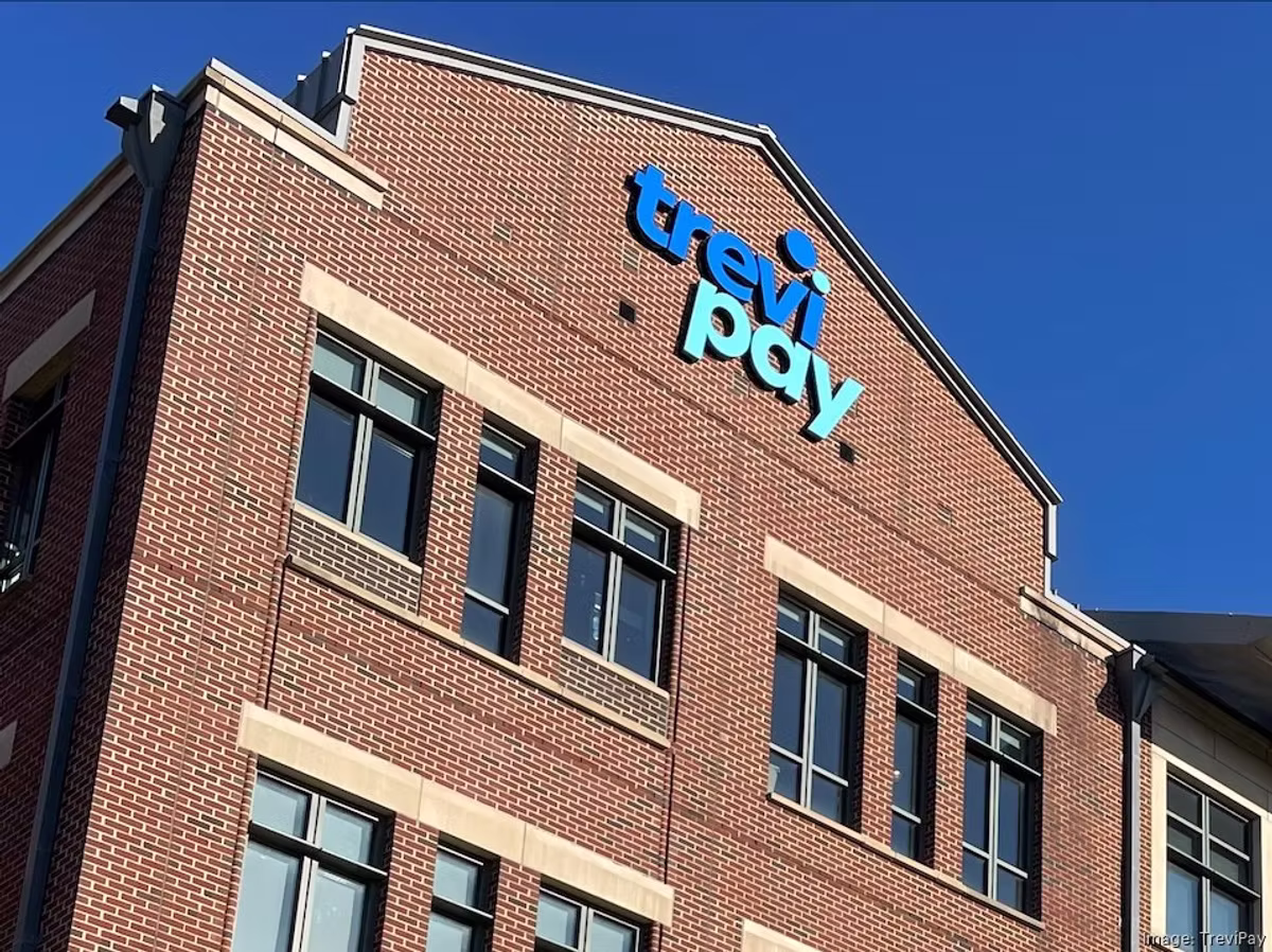 The TreviPay logo mounted on the brick facade of an office building against a clear blue sky.